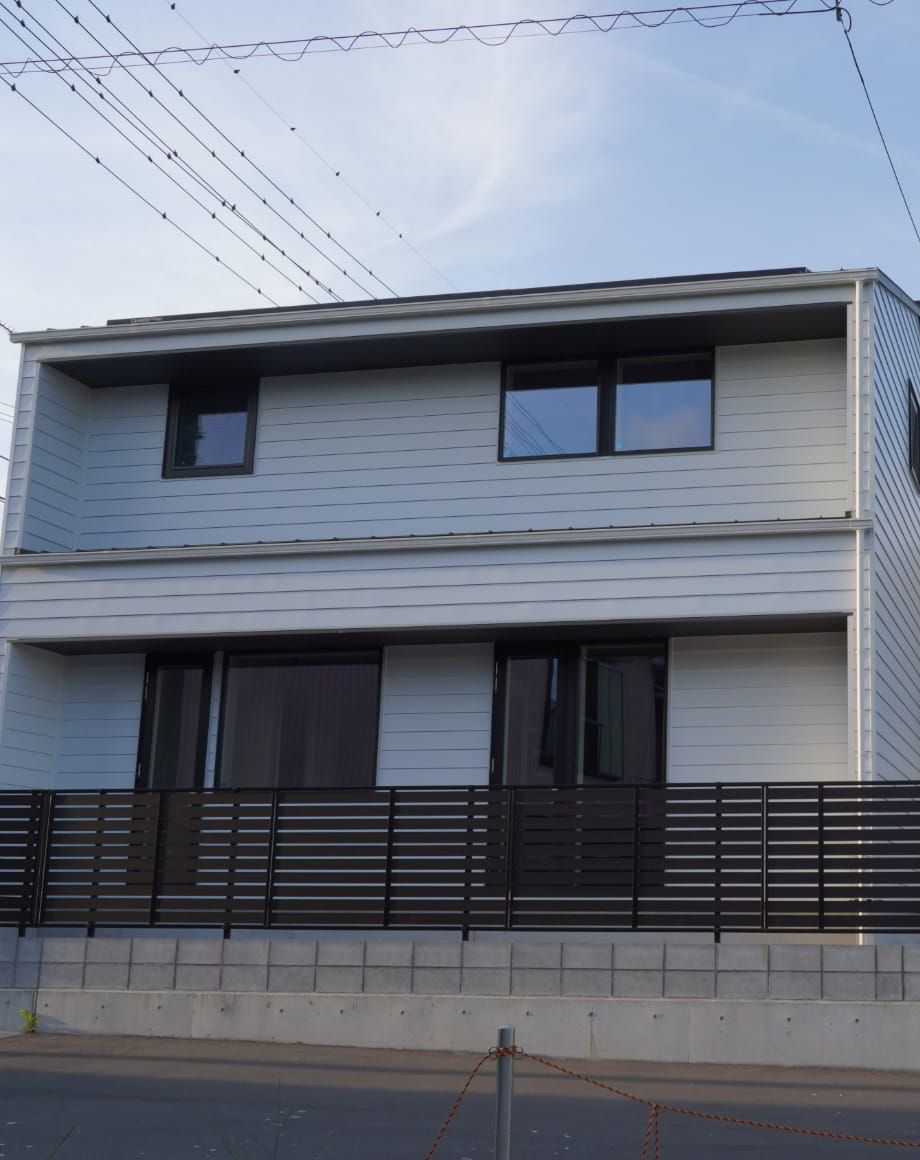 白い外壁と黒いサッシが調和するモダンな二階建て住宅。直線的なデザインが印象的な外観