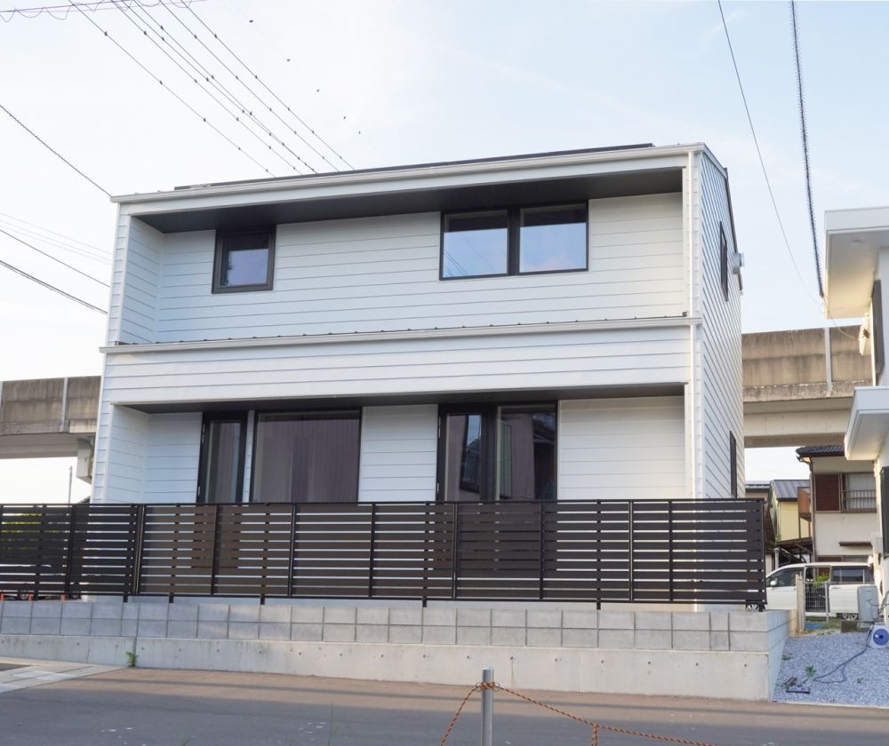 白い外壁と黒いサッシが調和するモダンな二階建て住宅。直線的なデザインが印象的な外観